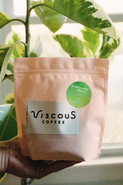 Overdamped Decaf coffee bag held among green leaves