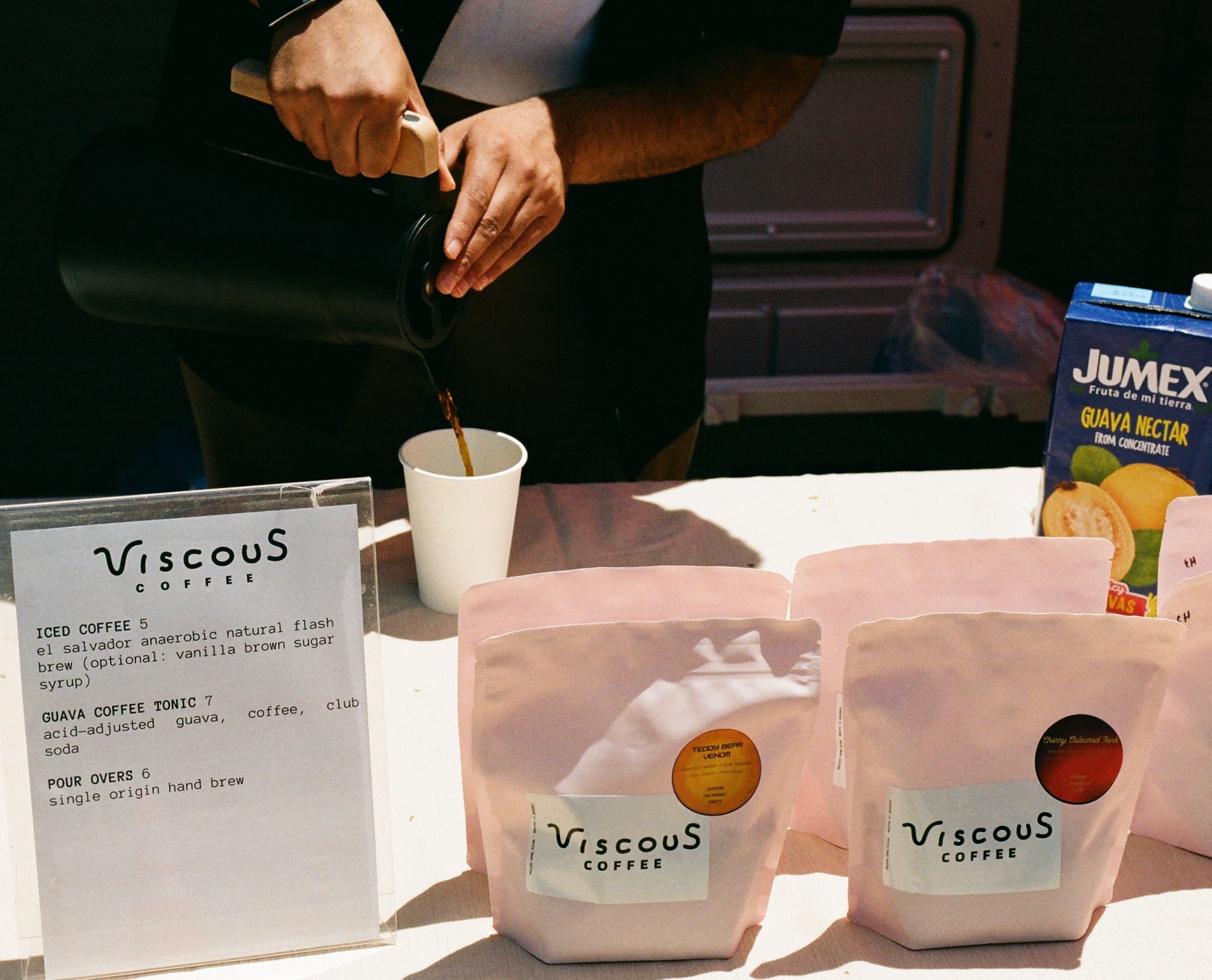 Viscous Coffee being poured at a pop-up table with bags of roasted coffee