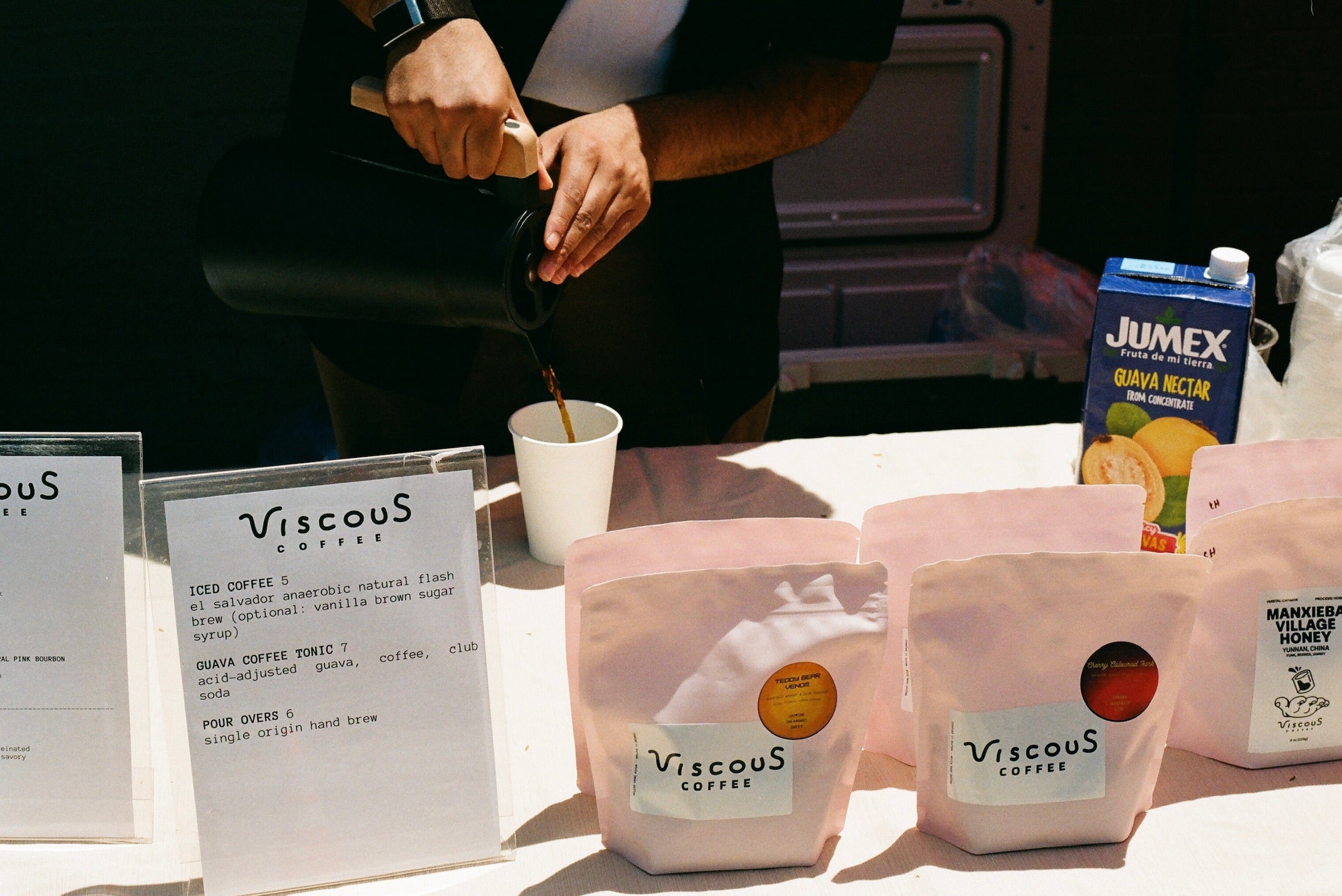 Viscous Coffee being poured at a pop-up table with bags of roasted coffee